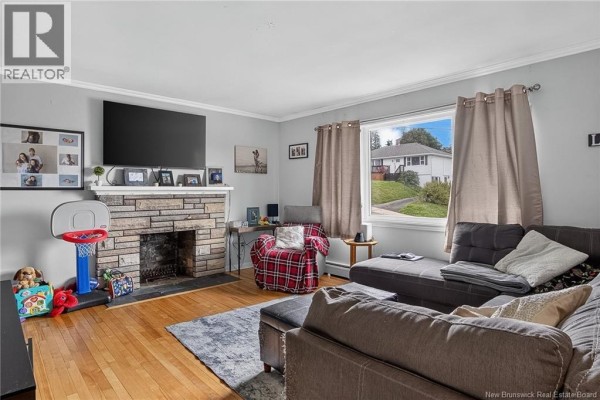 Living room with a stone fireplace, hardwood floors, a large sectional sofa, and a bay window. - 54-56 Northumberland Avenue, Saint John