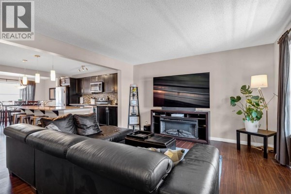 Living room with a large black sectional sofa, fireplace, and view into the kitchen area. - 54 Autumn View Se, Calgary