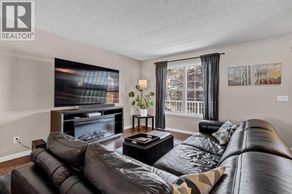 Living room featuring a large television, fireplace, sectional sofa, and window with blinds. - 54 Autumn View Se, Calgary