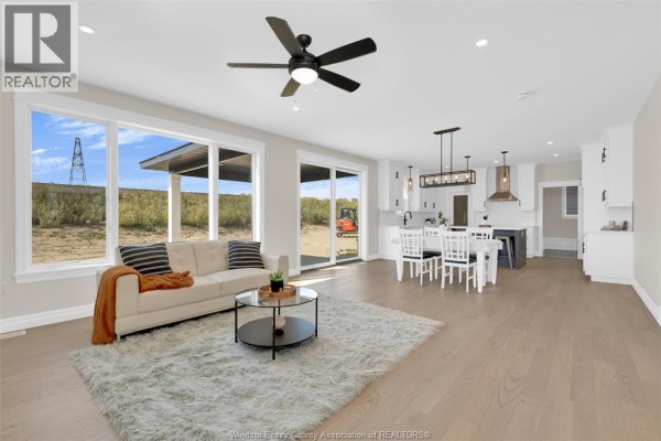 Open concept living room and kitchen with large windows, beige sofa, and white dining set. - 54 Belleview Drive, Kingsville
