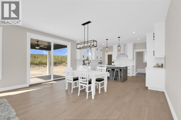 Dining area and kitchen with white table, island with pendant lights, and sliding glass doors. - 54 Belleview Drive, Kingsville