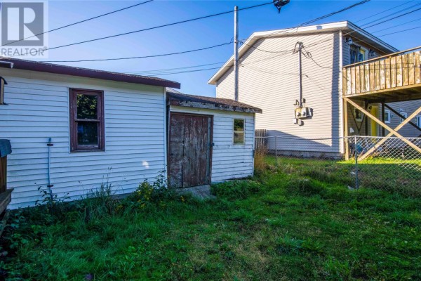 Backyard view of a small white shed with a weathered wooden door next to a chain-link fence. - 54 Cherrigton Street, St  John S