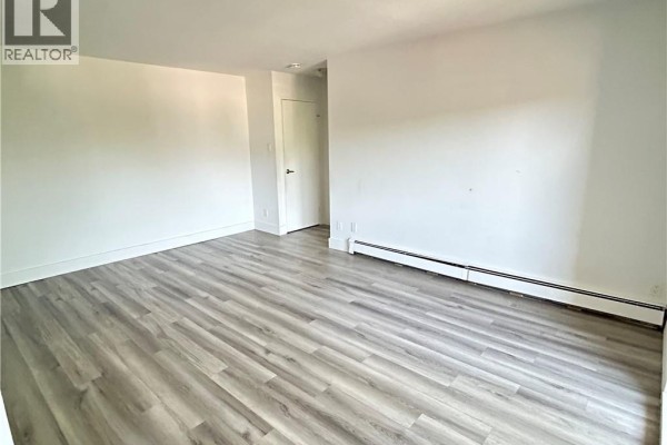 Living room with white walls, grey wood-look flooring, and a long baseboard heater. - 54 Country Hill Drive Unit# 318, Kitchener