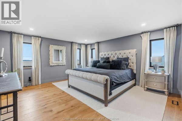 Bedroom with tufted bed, ornate mirror, and wood floors - 54 Dundee Drive West Chatham