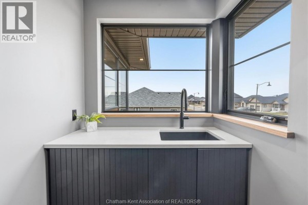 Modern kitchen sink with black faucet and white countertop under large window - 54 Dundee Drive West Chatham