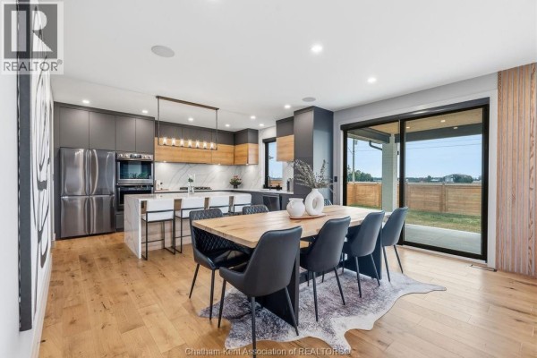 Modern dining room with a wood table and six chairs, adjacent to a sleek kitchen with stainless steel appliances - 54 Dundee Drive West Chatham
