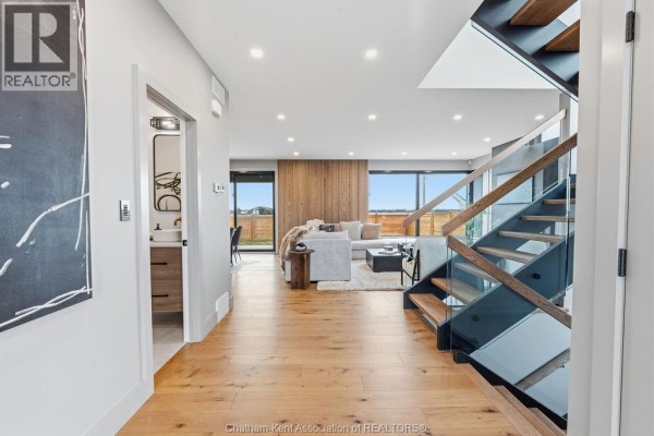 Modern hallway with hardwood floors, glass staircase, and living area view - 54 Dundee Drive West Chatham