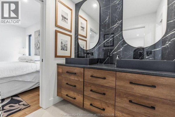 Modern bathroom with dual vessel sinks, wood vanity, marble tile, and oval mirror - 54 Dundee Drive West Chatham