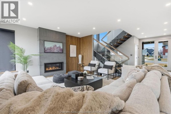 Living room featuring a sectional sofa, gas fireplace, wood accent wall, and open staircase with glass railings. - 54 Dundee Drive West, Chatham