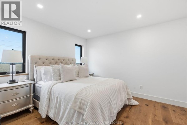 Bedroom with tufted headboard, large windows, and hardwood floors - 54 Dundee Drive West Chatham