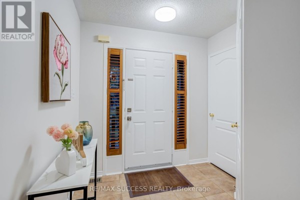 Tiled entryway with a white door, wooden shutters, and a console table. - 54 Ferncroft Place, Brampton