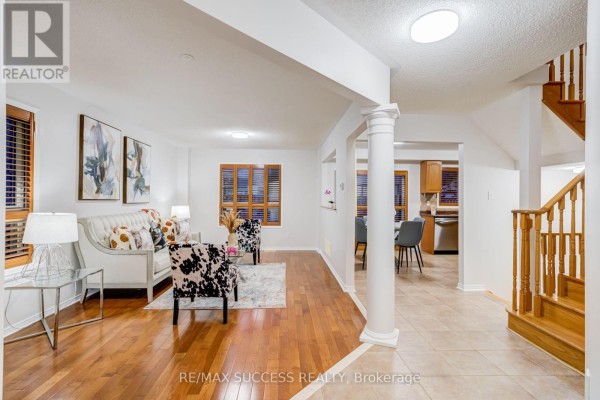 Living room with hardwood floors, white sofa, accent chairs, and view to dining area. - 54 Ferncroft Place, Brampton