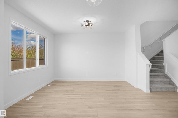 Bright living area with a large window, light wood floors, white walls, and carpeted stairs. - 54 Lemon Cl, Spruce Grove