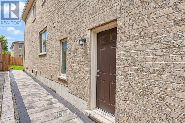 Side view of a brick house with a brown door and windows on a paved walkway. - 54 Mohandas Drive, Markham