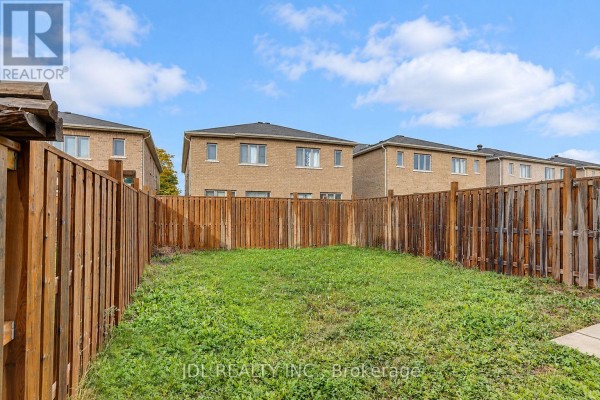 Backyard view of a green lawn enclosed by a wooden fence with houses in the background. - 54 Mohandas Drive, Markham