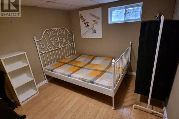 Basement bedroom with a white metal bed frame, plaid bedding, and a small bookshelf. - 54 Painswick Crescent, Toronto