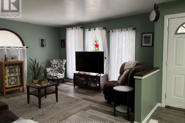 Living room with sage green walls, a dark brown sofa, patterned armchair, and a television on a media stand. - 54 Redwing Ave, Manitouwadge