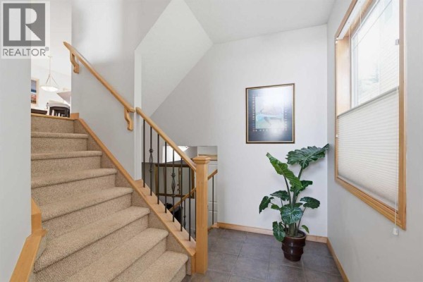 Carpeted staircase with wooden banisters leading to the second floor. - 54 Rockyledge Rise Nw, Calgary