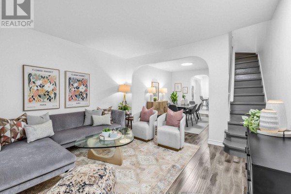 Living room with a grey sectional sofa, two cream armchairs, a glass coffee table, and artwork. - 54 Roseheath Avenue, Toronto