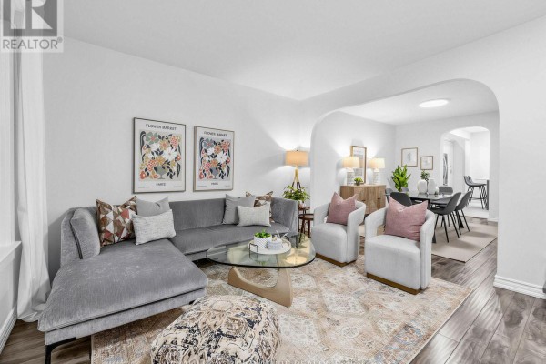 Living room with a grey sectional sofa, two cream armchairs, a glass coffee table, and artwork. - 54 Roseheath Avenue, Toronto