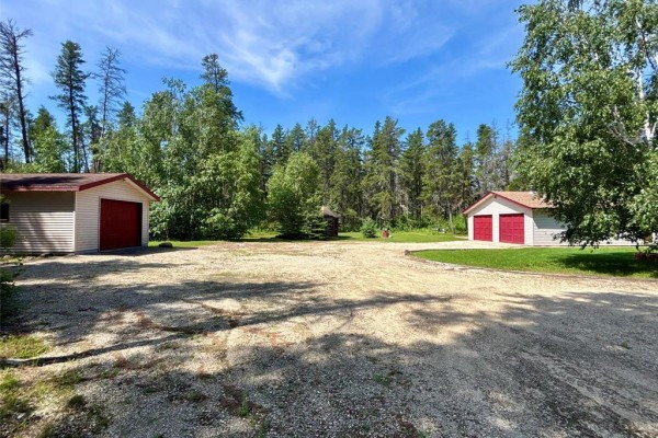 View of a gravel driveway with two detached garages and surrounding trees. - 54 Steck Drive, Belair