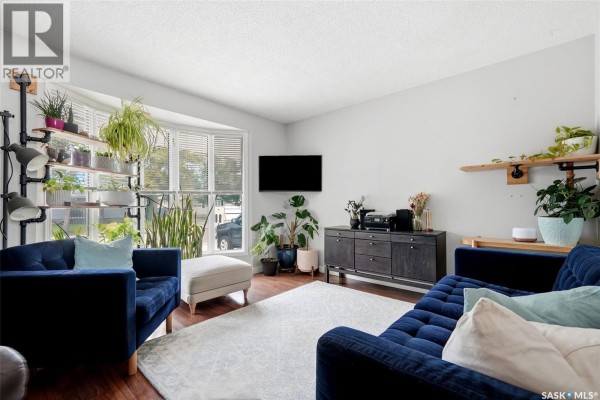 Living room with navy blue tufted couches, a bay window, and wood-look flooring. - 54 Trudelle Crescent, Regina