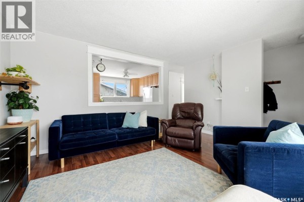 Living room with blue couches, a brown recliner, a pass-through window to the kitchen. - 54 Trudelle Crescent, Regina