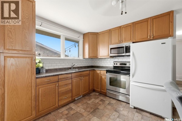 Kitchen with oak cabinets, stainless steel appliances, white subway tile backsplash, and vinyl flooring. - 54 Trudelle Crescent, Regina