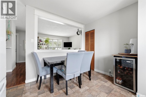 Dining area with a stone-top table, four upholstered chairs, and a wine fridge. - 54 Trudelle Crescent, Regina