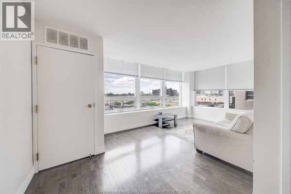 Apartment living room with dark hardwood floors, white walls, and large windows. - 540 Ouellette Avenue Unit# 5b, Windsor
