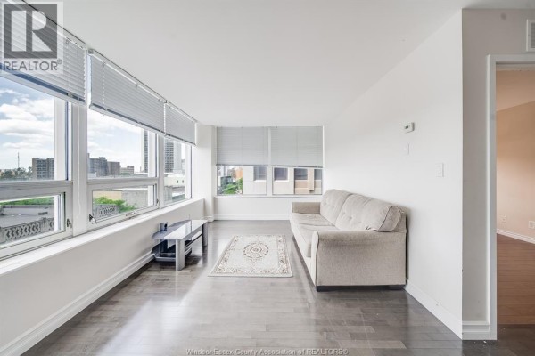 Living room featuring a beige sofa, coffee table, rug, and large windows with blinds. - 540 Ouellette Avenue Unit# 5b, Windsor
