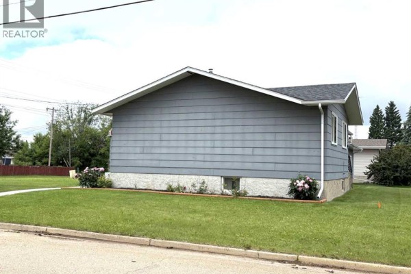 Rear side view of a gray house with a white foundation and green lawn, showing landscaping. - 5402 47 Avenue W, Forestburg