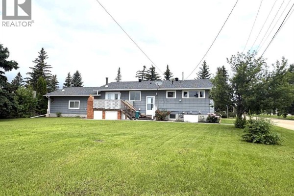 Back view of a gray house with a wooden deck, white railings, and a large green yard. - 5402 47 Avenue W, Forestburg