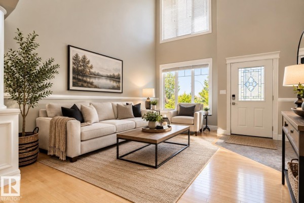 Living room with a large sectional sofa, coffee table, fireplace, and a high ceiling with large windows. - 5403 60 St, Beaumont