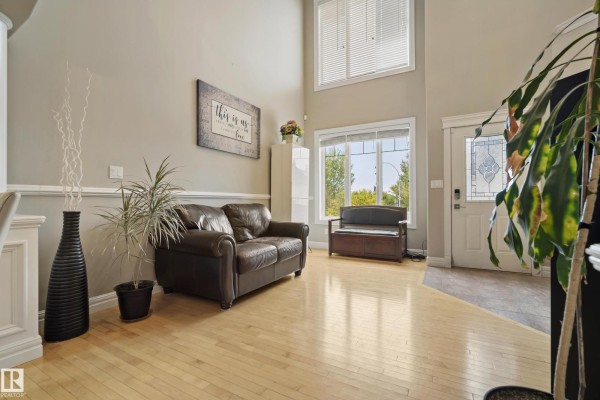 Living room with a dark brown leather sofa, large windows, and a white front door with glass inserts. - 5403 60 St, Beaumont