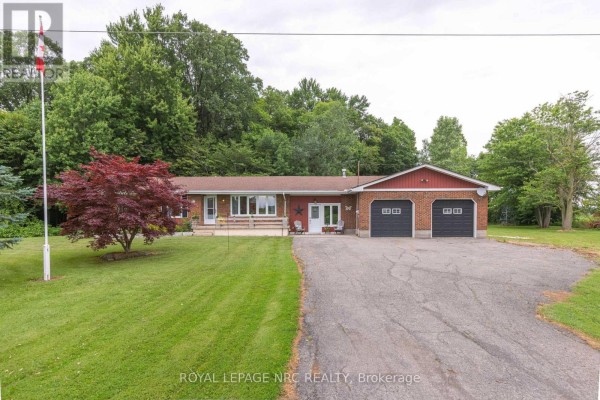 Front view of a red brick home with white trim, a paved driveway and mature trees. - 54038 Willford Road, Wainfleet