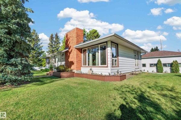 Side view of the house showcasing white siding, brick chimney, and large windows. - 5404 52 Av, Lamont
