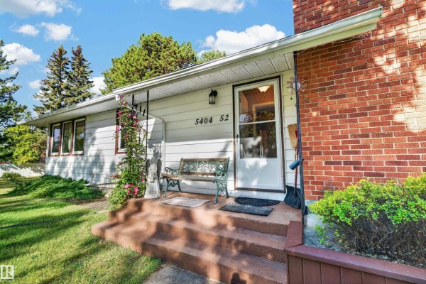 Front entrance with concrete steps leading to a white door, flanked by a green metal bench. - 5404 52 Av, Lamont