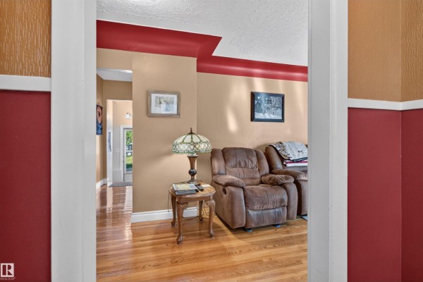 View from doorway into a living area with hardwood floors and taupe and red walls. - 5404 52 Av, Lamont