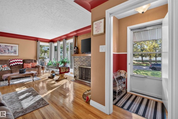 Living room with hardwood floors, fireplace, sofa, and a view of the front entrance. - 5404 52 Av, Lamont