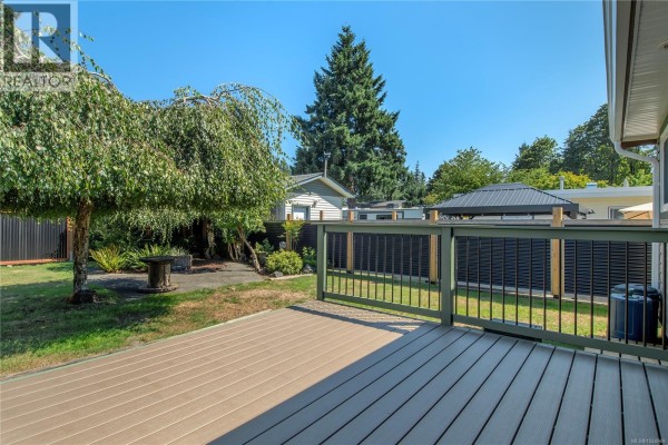 Deck view of the backyard with a weeping tree, grass, and dark slatted fencing. - 541 Colwyn St, Campbell River