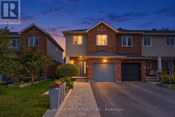 Exterior front view of a brick townhouse at dusk with exterior lights illuminated. - 541 Wild Shore Crescent, Ottawa