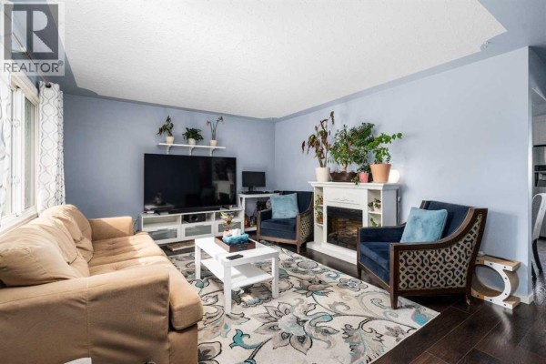 Living room with a sofa, chairs, fireplace, and television, featuring blue walls and a patterned rug. - 5410 Valentine Crescent Se, Calgary