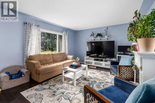 Living room with a sofa, chairs, fireplace, and television, featuring blue walls and a large window. - 5410 Valentine Crescent Se, Calgary