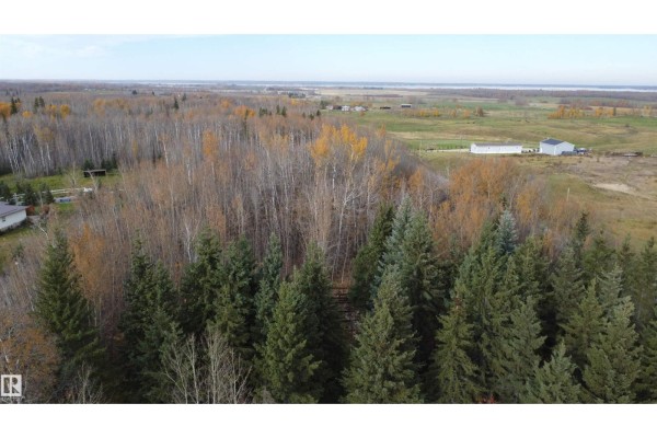 Aerial drone view over a vast forested area with scattered homes and agricultural fields under a blue sky. - 54104 Rr35, Rural Lac Ste  Anne County