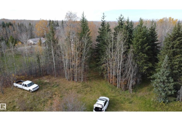Wide drone view of a rural property featuring a wooded area with two vehicles and a distant house. - 54104 Rr35, Rural Lac Ste  Anne County