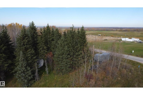 Overhead view of a treed lot adjacent to a road, with agricultural land and buildings in the distance. - 54104 Rr35, Rural Lac Ste  Anne County