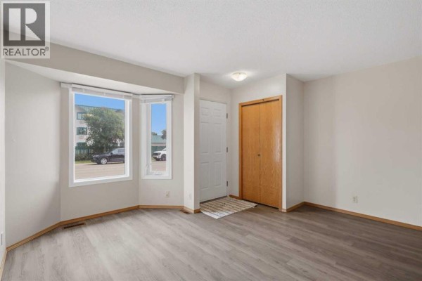 Interior view showing a living room with gray flooring, bay window, and closet. - 5414 45 Street, Lacombe