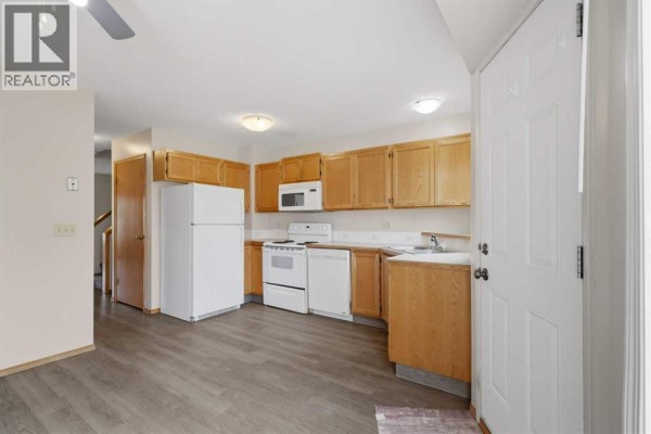Kitchen with light wood cabinets, white appliances, laminate flooring, and a sink. - 5414 45 Street, Lacombe