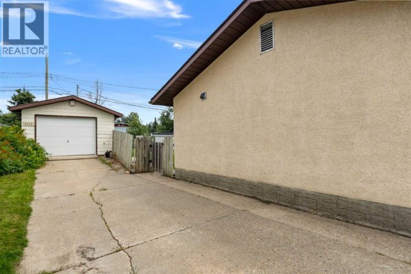 Concrete driveway leading to a white detached garage with a wooden fence. - 5415 Willock Crescent, Swan Hills